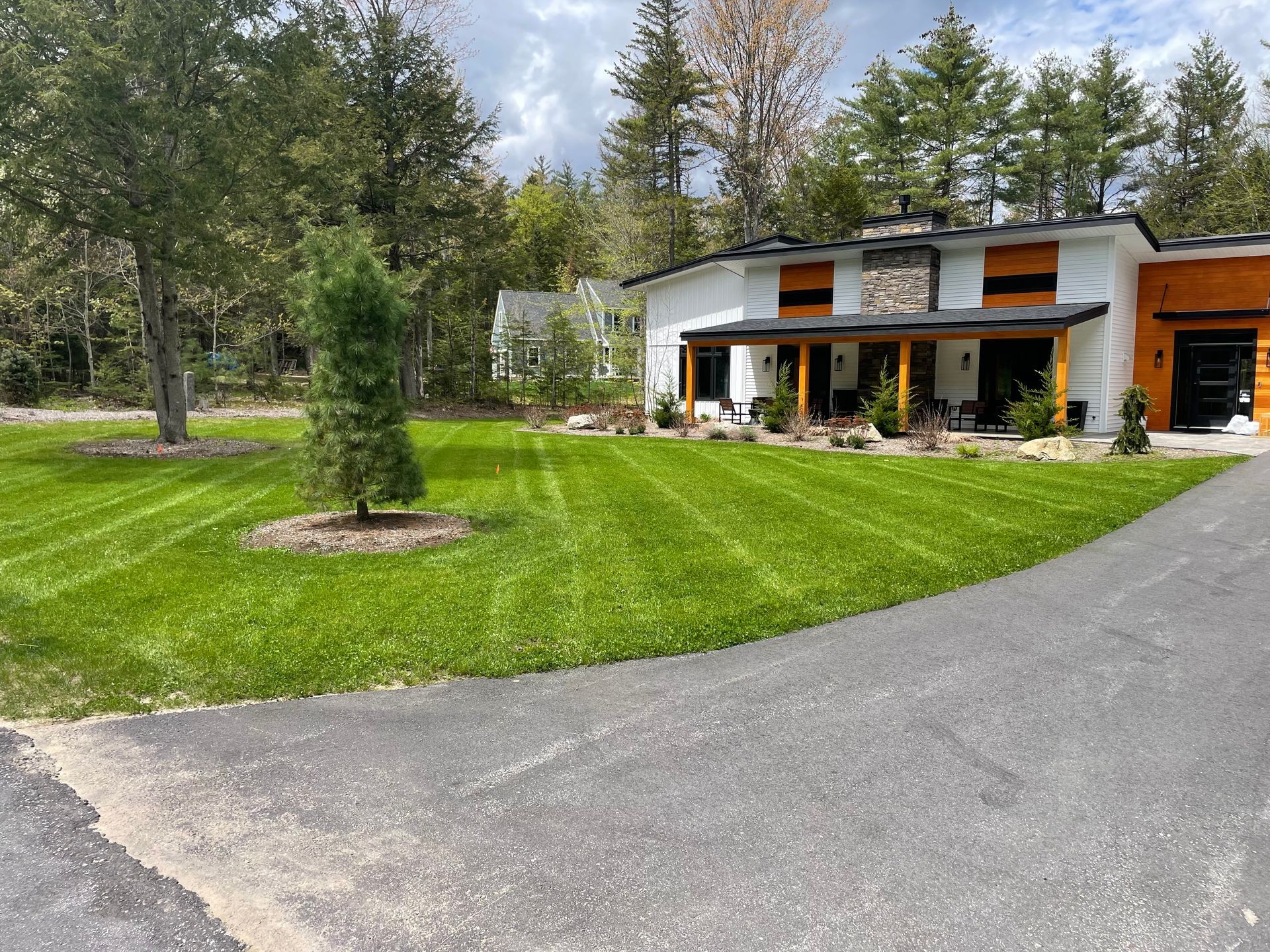 Modern house with large front lawn, surrounded by trees and a paved driveway.